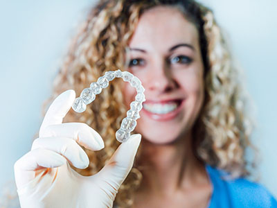 A woman holding up a transparent dental retainer with a smile on her face.