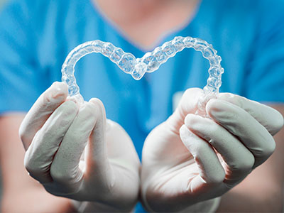 A person s hands holding a heart-shaped object with clear braces inside, set against a background featuring medical gloves and a blue surgical gown.